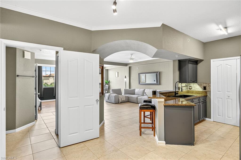 12955 Positano Circle, Unit 305 Naples, FL 34105 - Photo 3 of 10 Kitchen with a peninsula, dark stone countertops, a kitchen breakfast bar, a ceiling fan, and arched walkways