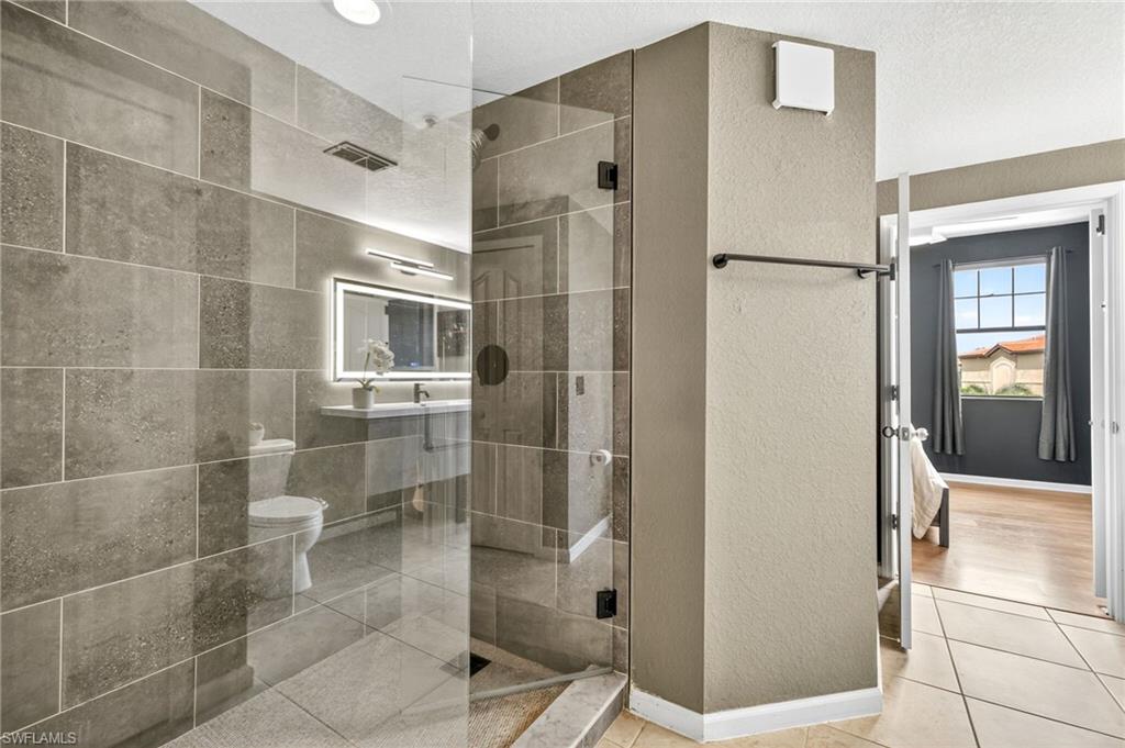 12955 Positano Circle, Unit 305 Naples, FL 34105 - Photo 7 of 10 Full bath featuring a textured wall, a shower stall, and light tile patterned floors