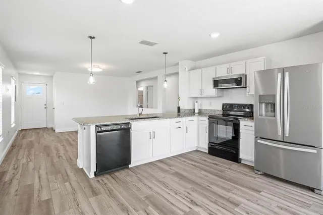 a kitchen with granite countertop a refrigerator oven a sink dishwasher and white cabinets with wooden floor