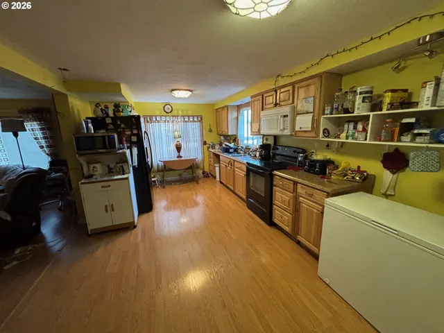 a kitchen with stainless steel appliances a stove a refrigerator white cabinets and couches with wooden floor