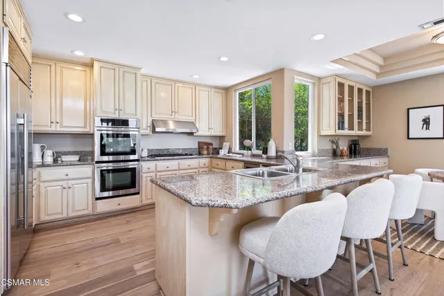 a kitchen with stainless steel appliances granite countertop a refrigerator a sink dishwasher a stove and white cabinets with wooden floor