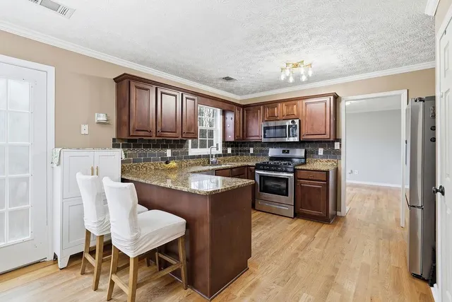 a kitchen with stainless steel appliances granite countertop a stove top oven a sink dishwasher a dining table and chairs with wooden floor