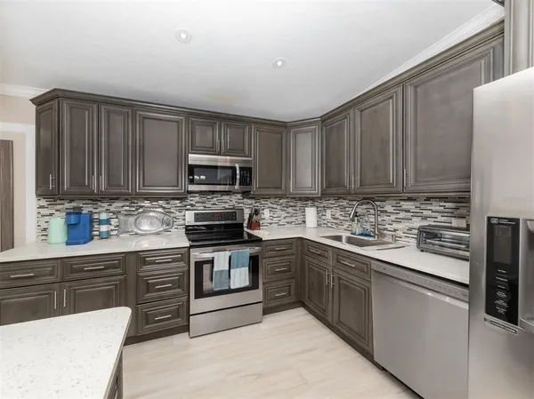 a kitchen with stainless steel appliances granite countertop a stove top oven a sink dishwasher and a refrigerator with wooden cabinets