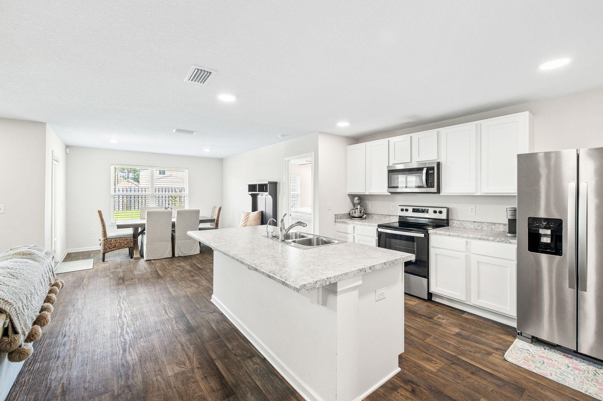 245 This Way Freeport, FL 32439 - Photo 4 of 46 a kitchen with stainless steel appliances a white stove top oven a refrigerator a dining table and chairs with wooden floor