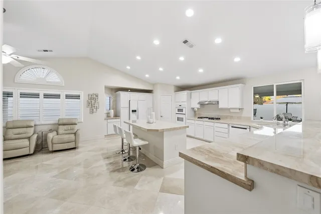 a large white kitchen with stainless steel appliances kitchen island granite countertop a sink and white cabinets