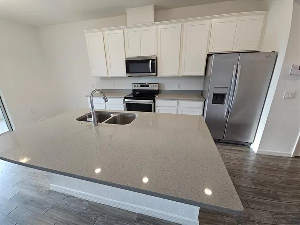 a kitchen with granite countertop a refrigerator a sink a stove a microwave and wooden floor