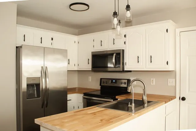 a kitchen with stainless steel appliances granite countertop a refrigerator a stove a sink dishwasher and white cabinets with wooden floor