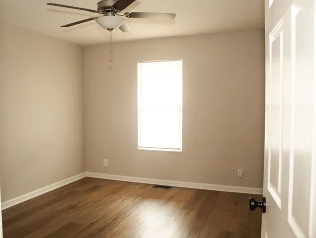 an empty room with wooden floor fan and windows