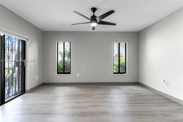 an empty room with wooden floor a ceiling fan and windows