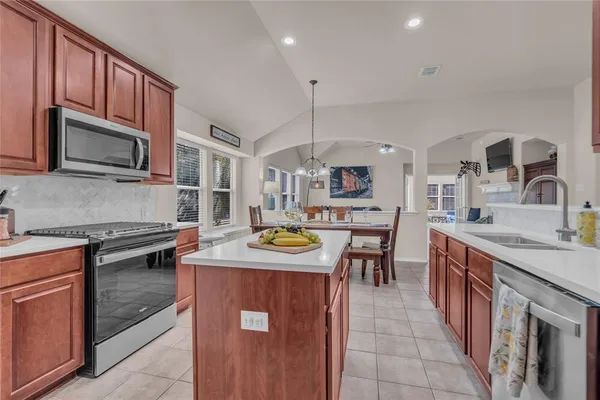 a kitchen with stainless steel appliances granite countertop a stove top oven a sink dishwasher a dining table and chairs with wooden cabinets