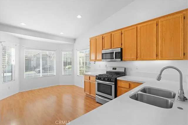 a kitchen with stainless steel appliances a stove a sink a microwave a refrigerator cabinets and a window