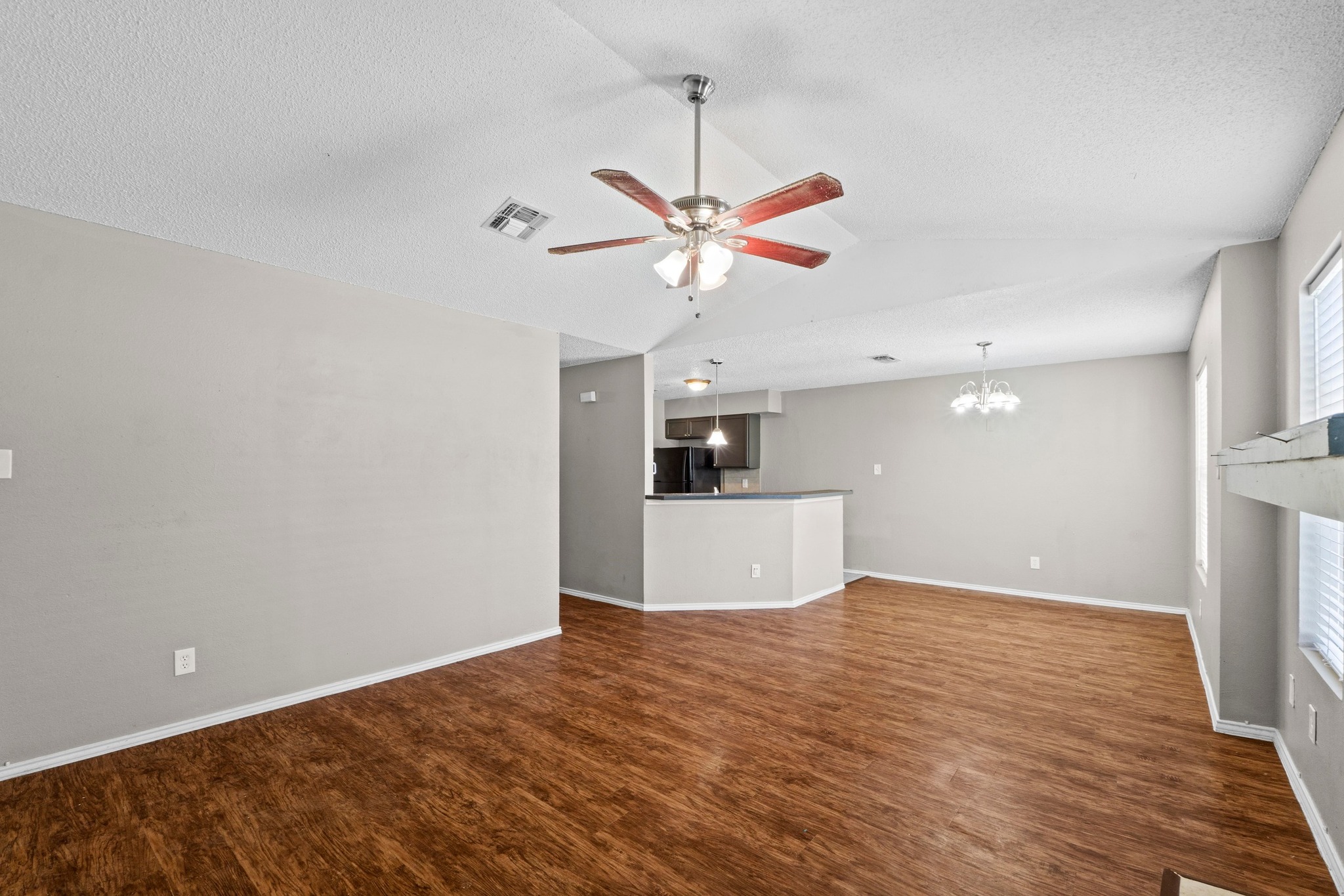 4208 Duval Road, Unit C Austin, TX 78759 - Photo 4 of 28 Unfurnished living room with wood finished floors, a chandelier, a ceiling fan, vaulted ceiling, and a textured ceiling