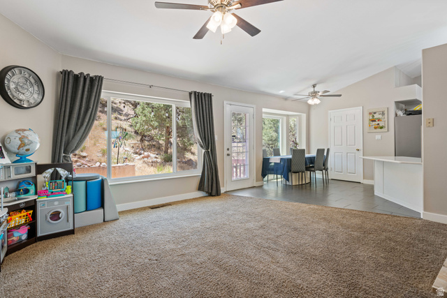 790 East Fiddlers Canyon Road Cedar City, UT 84721 - Photo 6 of 35 Spacious living area featuring ample natural light, vaulted ceilings, two ceiling fans, mixed flooring with carpet and tile, and a door leading to exterior space