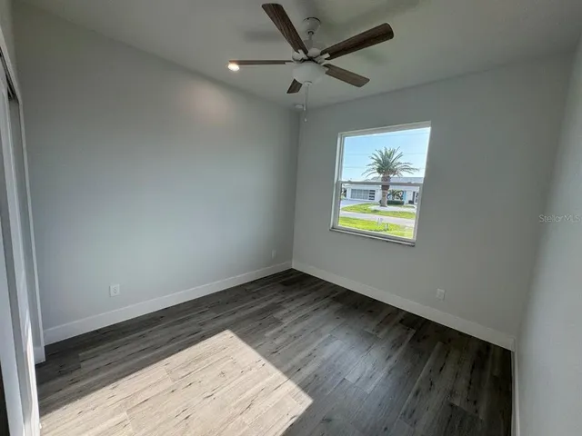 an empty room with wooden floor ceiling fan and windows