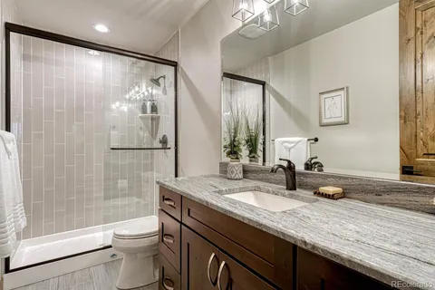 a bathroom with a granite countertop sink a toilet a mirror a vanity and shower