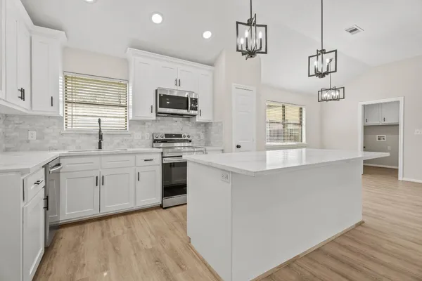a open kitchen with stainless steel appliances granite countertop a stove a sink dishwasher a refrigerator and a microwave oven with white cabinets