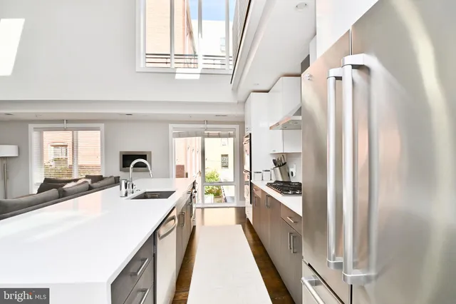 a large white kitchen with a lot of counter top space a sink a refrigerator and windows