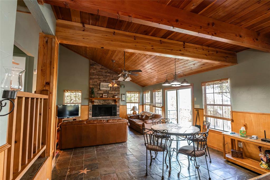 698 Storey Road Nocona, TX 76255 - Photo 26 of 34 Dining room with a stone fireplace, a wood ceiling with exposed beams, a ceiling fan, stone tile flooring, and a wainscoted wall