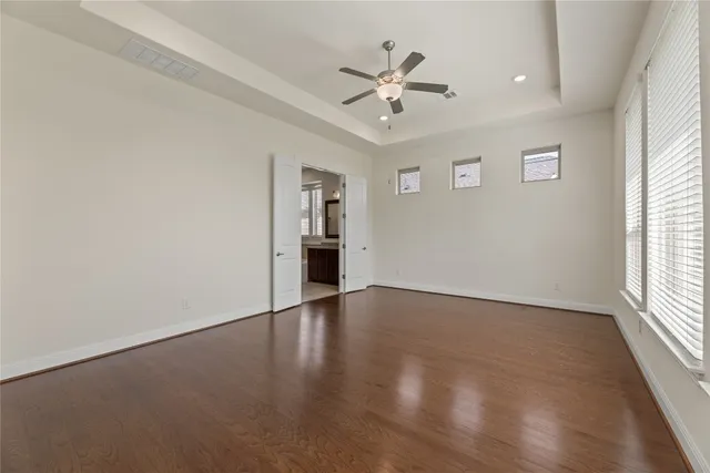 an empty room with wooden floor chandelier fan and windows