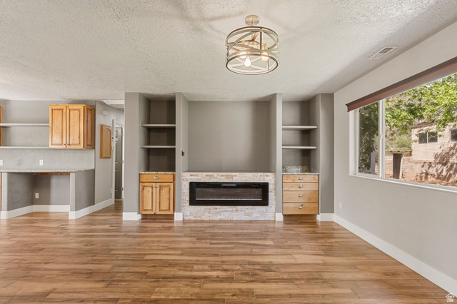 55 Spring Drive Toquerville, UT 84774 - Photo 7 of 36 Unfurnished living room featuring built in features, a textured ceiling, a stone fireplace, and light wood-style flooring