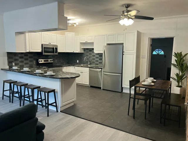 a kitchen with stainless steel appliances granite countertop a stove a refrigerator a sink a dining table and chairs with wooden floor