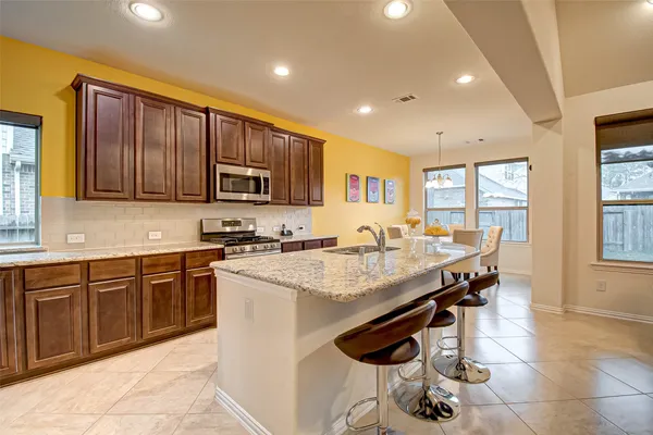 a open kitchen with stainless steel appliances granite countertop a stove top oven a sink dishwasher a dining table and chairs with wooden floor