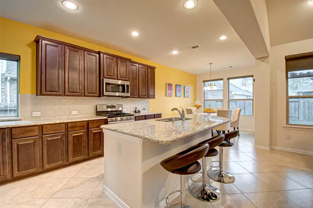 a open kitchen with stainless steel appliances granite countertop a stove top oven a sink dishwasher a dining table and chairs with wooden floor