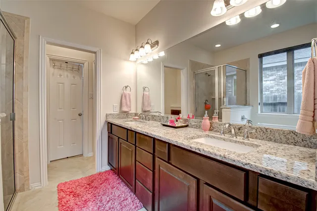 a bathroom with a granite countertop double vanity sink a mirror and a shower