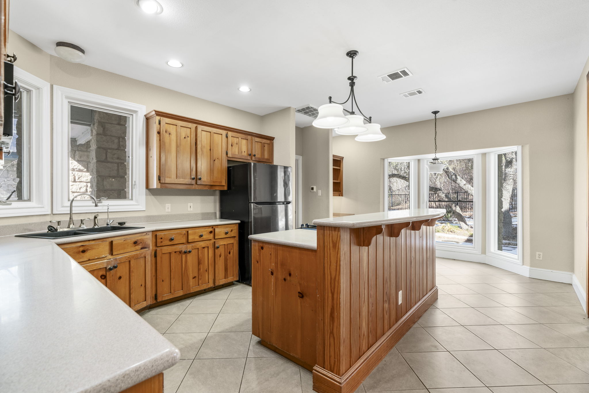 310 County Road 317 Georgetown, TX 78626 - Photo 8 of 40 Kitchen featuring light countertops, a kitchen island, decorative light fixtures, freestanding refrigerator, and brown cabinetry