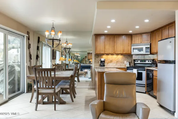 a kitchen with stainless steel appliances kitchen island granite countertop a dining table chairs refrigerator and microwave