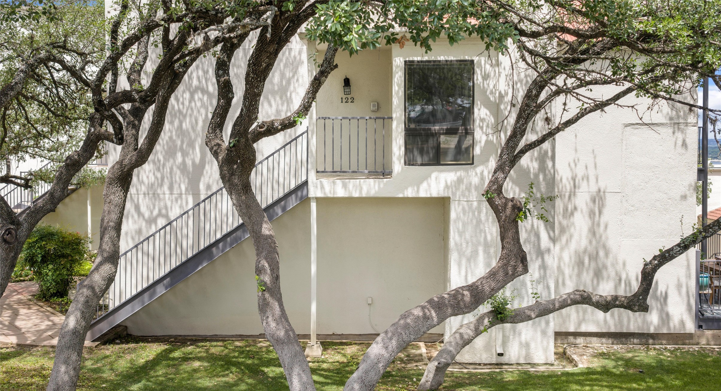 2918 Ranch Road 620 North, Unit C122 Austin, TX 78734 - Photo 1 of 36 The property features a private balcony with a metal railing, a prominent exterior staircase, and mature trees providing shade to the lawn area