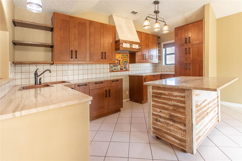 308 Sanders Road Denton, TX 76210 - Photo 14 of 31 Kitchen featuring wood cabinetry, light-toned countertops, white tiled backsplash, and a central island with a stone-finish top