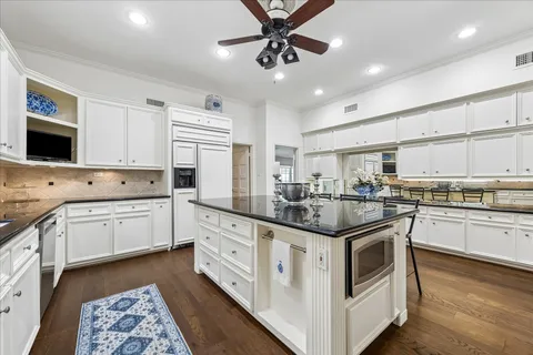 a kitchen with stainless steel appliances kitchen island granite countertop a stove a sink a refrigerator and white cabinets with wooden floor