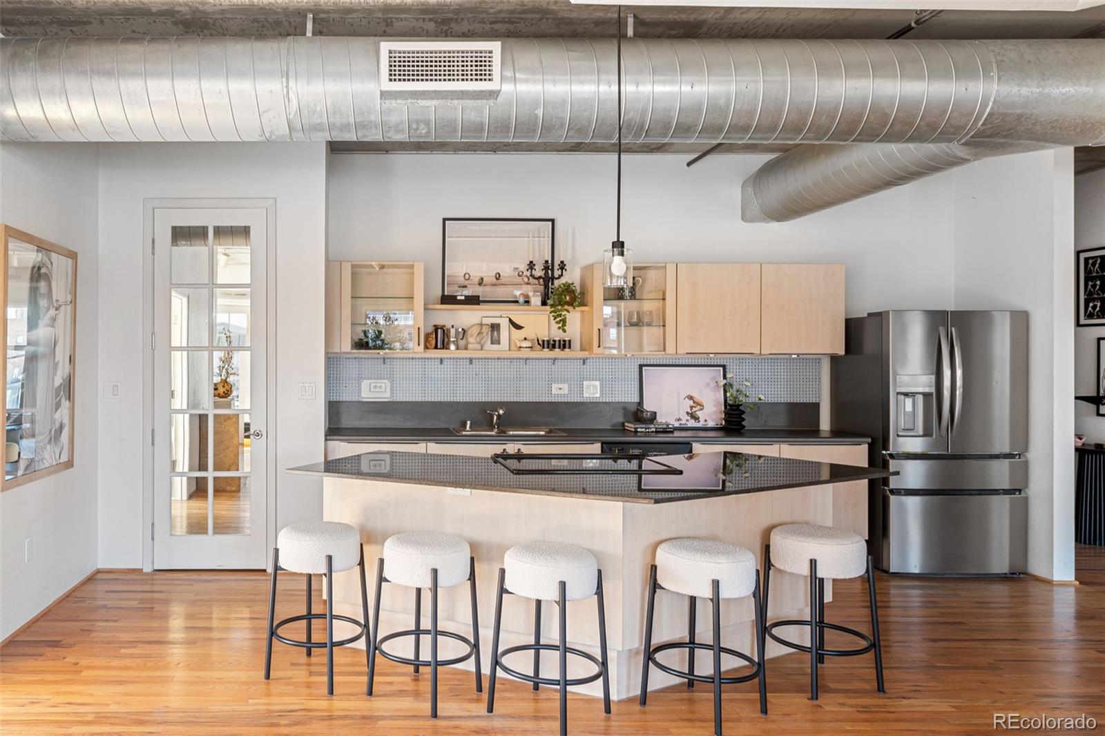 1499 Blake Street, Unit 6A Denver, CO 80202 - Photo 19 of 46 a kitchen with stainless steel appliances kitchen island granite countertop a stove a refrigerator and white cabinets with wooden floor