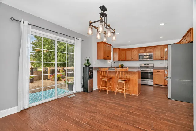 a kitchen with stainless steel appliances kitchen island granite countertop a refrigerator a stove and a wooden floor