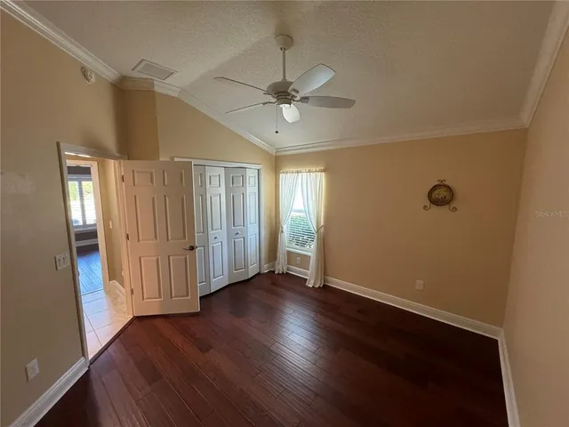 a view of an empty room with wooden floor and a ceiling fan