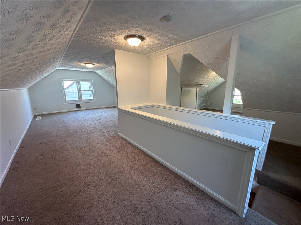 18230 Libby Road Maple Heights, OH 44137 - Photo 26 of 39 Additional living space featuring lofted ceiling, carpet, baseboards, and a textured ceiling