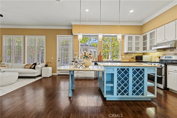a living room with kitchen island granite countertop wooden floor a large window and a sink