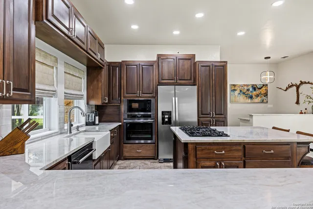 a kitchen with stainless steel appliances kitchen island granite countertop a refrigerator a stove and a sink with wooden cabinets