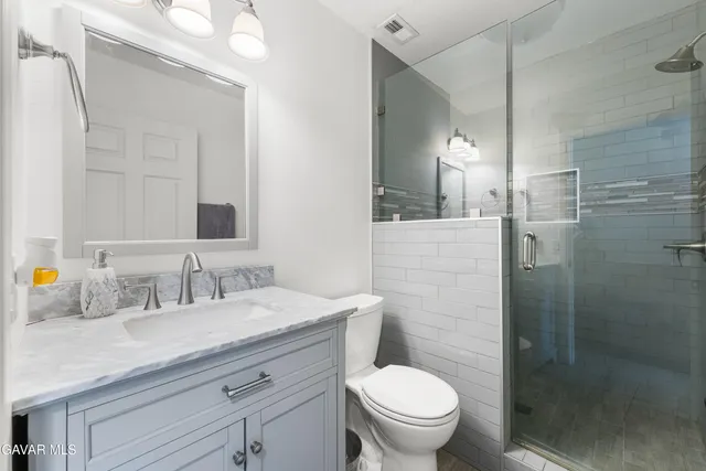 a bathroom with a granite countertop sink a toilet a mirror and shower