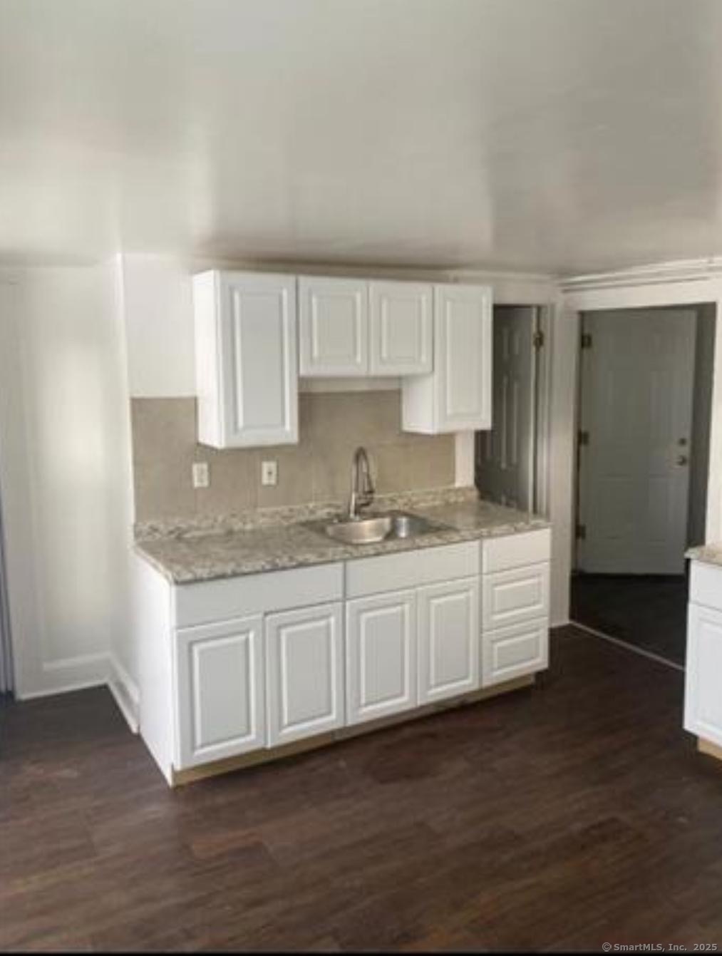 a white kitchen with granite countertop a sink and dishwasher with wooden floor