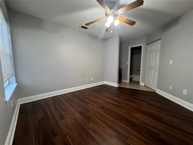 a view of an empty room with wooden floor and a ceiling fan