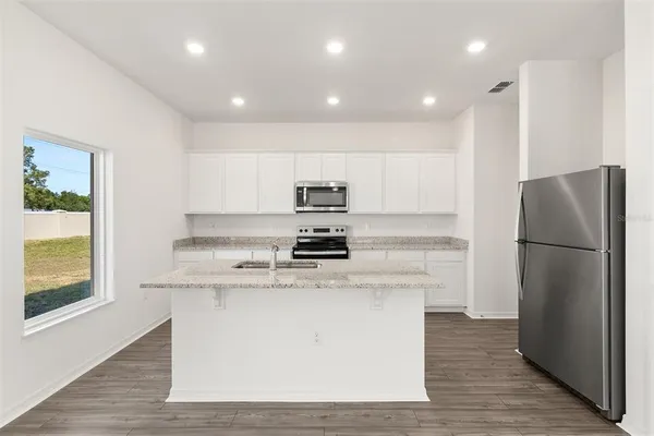 a kitchen with stainless steel appliances granite countertop a refrigerator a stove a sink and a oven with wooden floor