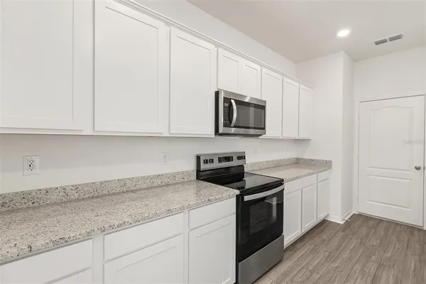 a kitchen with granite countertop white cabinets stainless steel appliances and a wooden floor