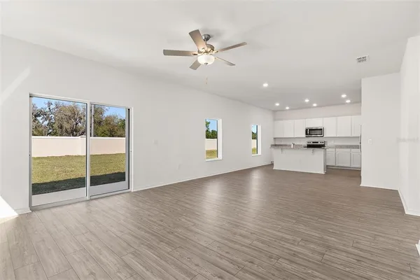 a view of an empty room with wooden floor and a kitchen