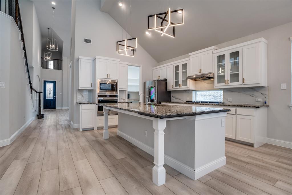 2811 Killdeer Trail Prosper, TX 75078 - Photo 7 of 36 Kitchen featuring backsplash, glass fronted cabinets, stainless steel appliances, white cabinets, and vaulted ceiling