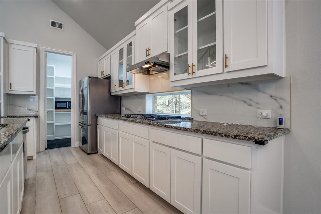 2811 Killdeer Trail Prosper, TX 75078 - Photo 8 of 36 Kitchen featuring lofted ceiling, white cabinetry, glass insert cabinets, light wood-type flooring, and dark stone countertops
