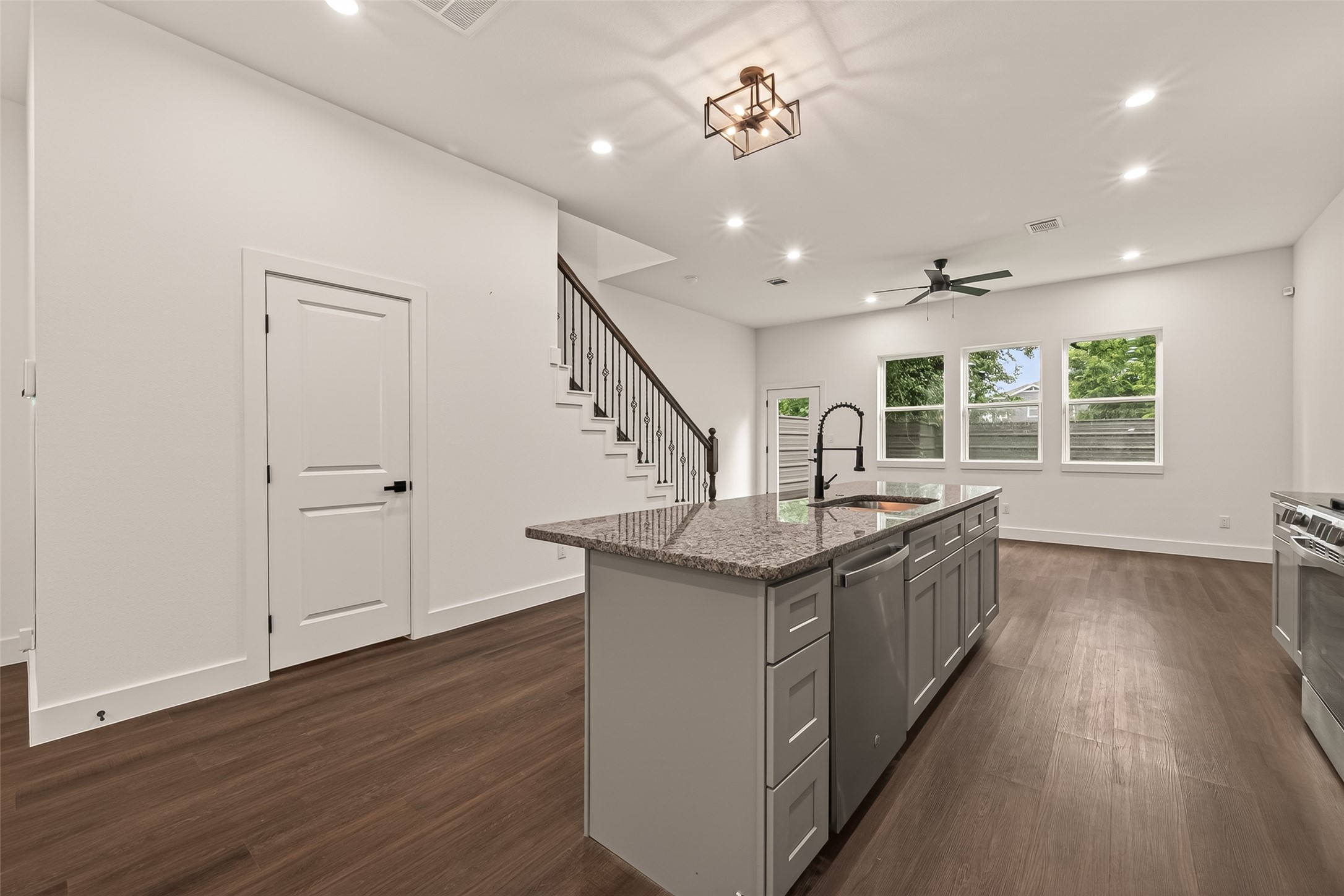 6808 Madrid Street Houston, TX 77021 - Photo 7 of 31 This photo showcases a modern open-plan kitchen and living area featuring sleek engineer wood floors, a large island with granite countertops, stainless steel appliances, and recessed lighting. The space is brightened by ample natural light from multiple windows, and there's a contemporary ceiling fan for added comfort.