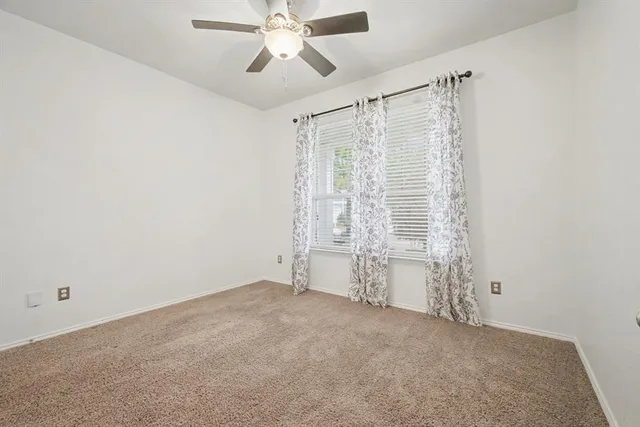 an empty room with chandelier fan and windows