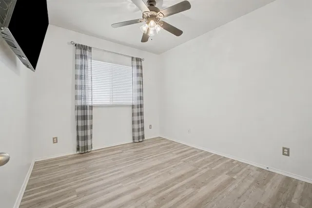 a view of empty room with wooden floor and fan